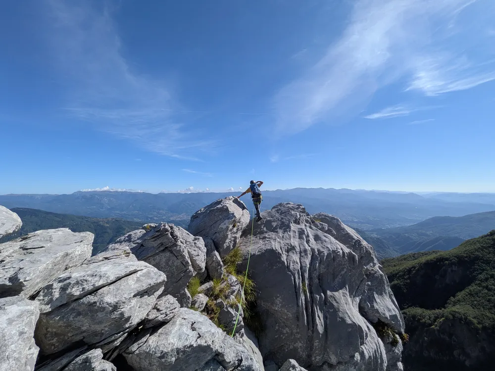 Alpinista cammina sul filo della ucresta dei denti alla pania secca nelle Alpi Apuane durante il corso di alpinismo su creste rocciose, con la valle e un paese sullo sfondo